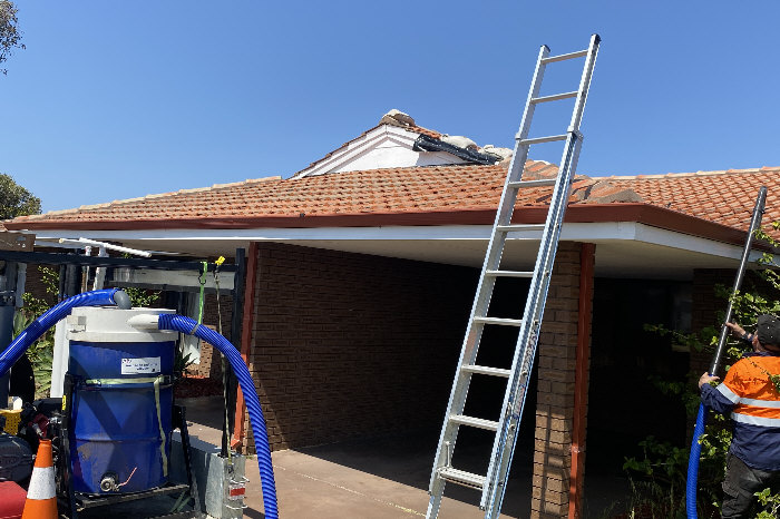 Elevation of house with ladder against it and trailer mounted vacuum gutter cleaner in foreground