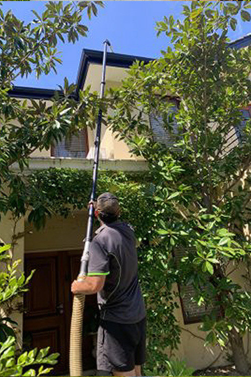 Photo of a worker using extended gutter cleaning equipment, with a long pole extension, working on 2 story house