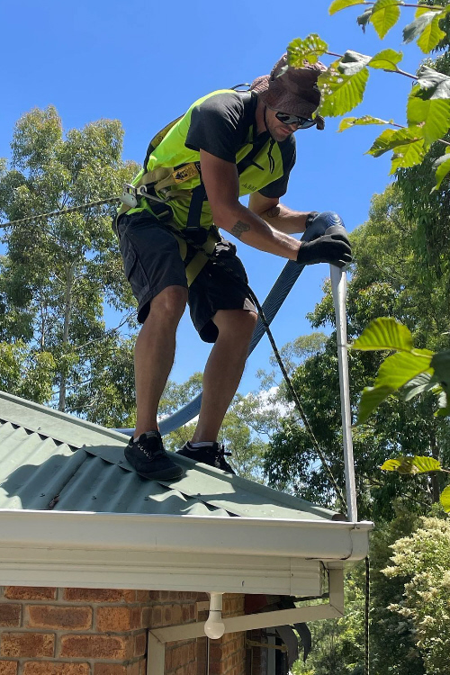 Man in high vis gear, working on roof with vacuum gutter cleaning equipment, removing leaves fromgutter