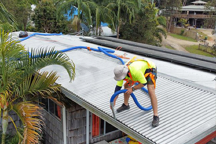 Man on roof using vacuum gutter cleaner to remove leaves and debris from gutter with extended hose and fittings